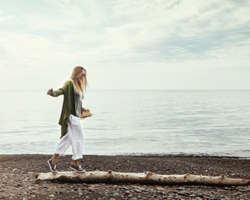 woman walking on large stick on beach